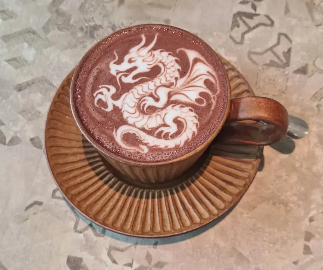 Cawan coklat panas dengan seni latte berbentuk naga berlingkar